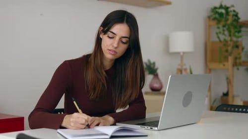 Junge Frau arbeitet mit Laptop und Notizen an einem Schreibtisch